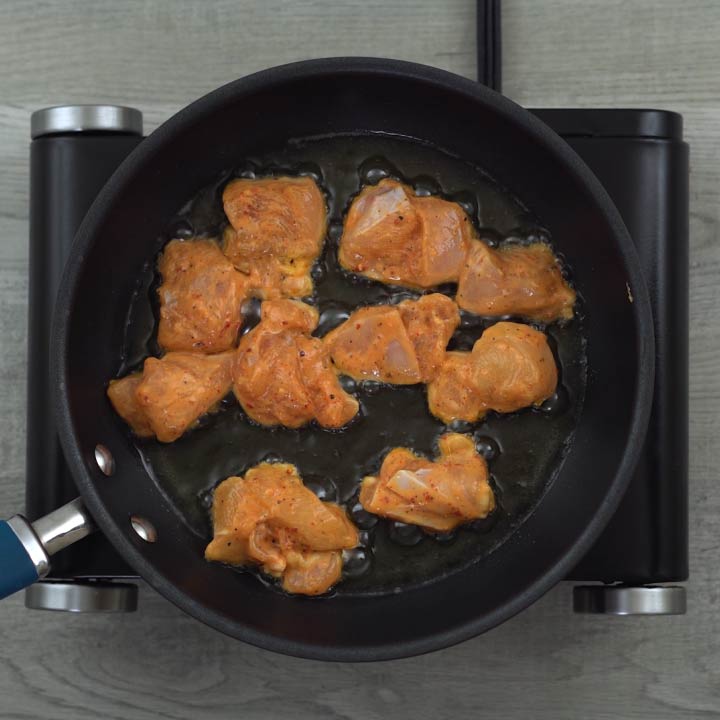 frying the marinated chicken in a pan