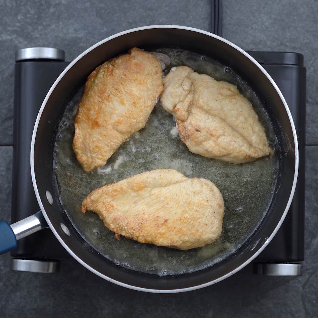 Chicken breast flipped and frying in oil