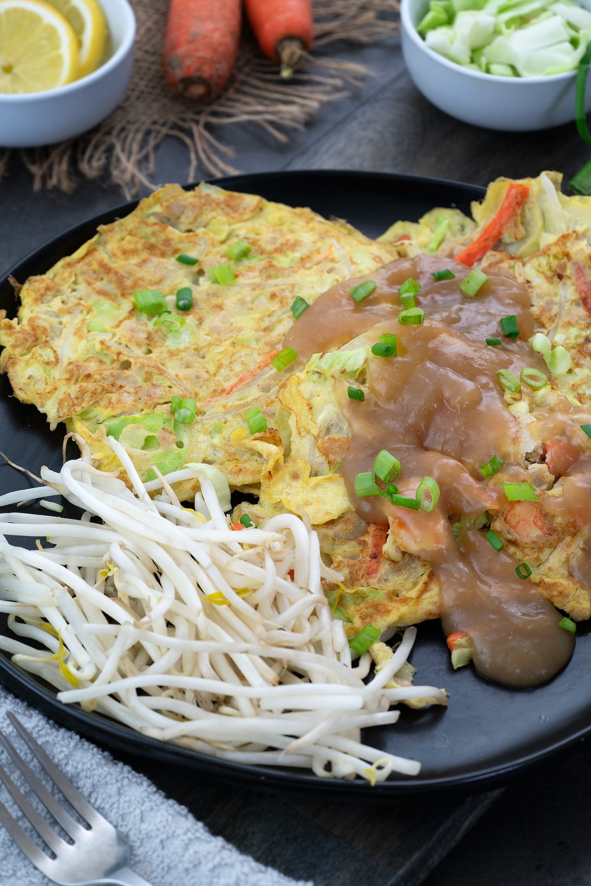 Egg Foo Young served in a black plate with lemon and cabbage in a cup nearby