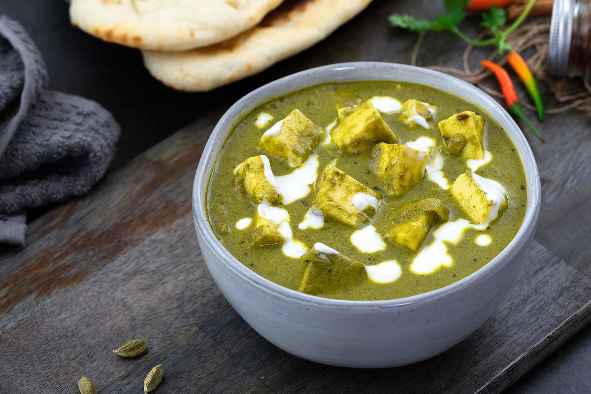 Palak Paneer served in a white bowl and placed on a grey table with naan nearby