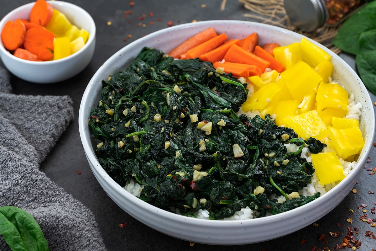 Sauteed spinach in a white bowl with carrot and yellow bell pepper pieces