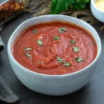 Marinara Sauce in a white bowl placed on a grey table with few ingredients around