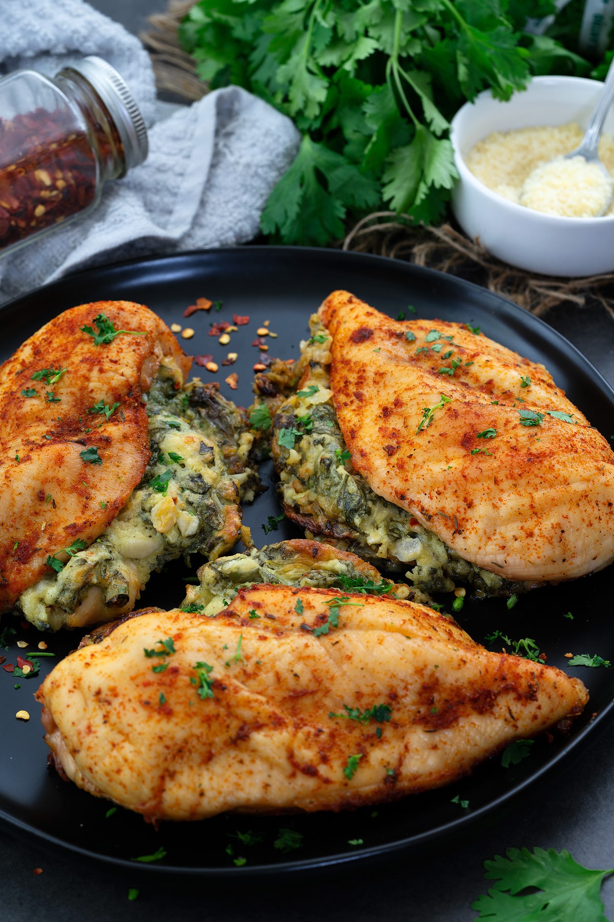 3 Spinach stuffed chicken breasts in a black plate with cheese alongside in a cup